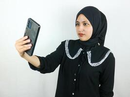 schön jung asiatisch Frau tragen Hijab lächelnd und Selfie nehmen Bilder durch ihr Handy, Mobiltelefon Telefon foto