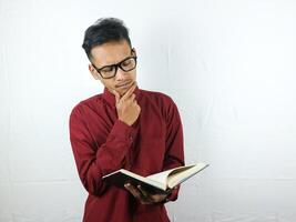Porträt von asiatisch Mann halten Buch mit Denken Gesicht Ausdruck foto
