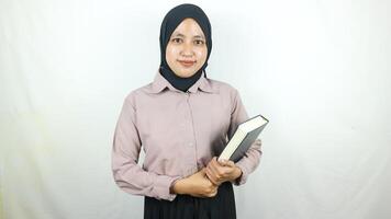 lächelnd jung asiatisch Muslim Schüler halten Buch, suchen beim Kamera isoliert auf Weiß Hintergrund. foto