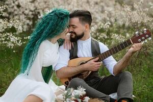 ein bärtig Bräutigam Theaterstücke ein besaitet Instrument und ein Mädchen sitzt im ein Frühling Wiese foto