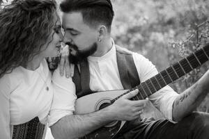 ein bärtig Bräutigam Theaterstücke ein besaitet Instrument und ein Mädchen sitzt im ein Frühling Wiese foto