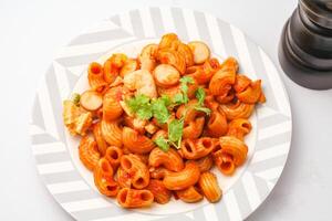 Makkaroni Pasta mit Tomate Soße und geschnitten Würstchen serviert auf ein Weiß Teller auf ein Blau Hintergrund. foto