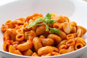 Makkaroni mit Tomate Soße und Petersilie im ein Weiß Schüssel serviert auf ein Weiß Teller foto