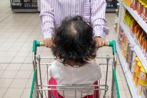 ein Mutter schieben ein Einkaufen Wagen Dan ihr Kind Sitzung im Wagen im Supermarkt foto
