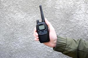 das Kerl ist halten ein Walkie-Talkie im seine Hand auf ein grau Hintergrund. foto