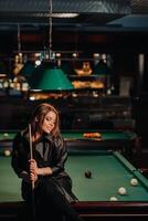 ein Mädchen mit ein Stichwort im ihr Hände sitzt auf ein Tabelle im ein Billard- Club.Russisch Billard foto