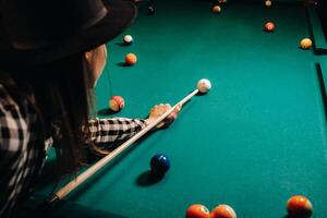 ein Mädchen im ein Hut im ein Billard- Verein mit ein Stichwort im ihr Hände Treffer ein Ball.spielen Schwimmbad foto