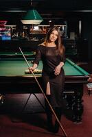 ein Mädchen im ein Hut im ein Billard- Verein mit ein Stichwort im ihr Hände.Pool Spiel foto