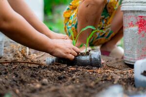 wenig Mädchen und Mama wachsen Pflanzen im Töpfe von recycelt Wasser Flaschen im das Hinterhof. recyceln Wasser Flasche Topf, Gartenarbeit Aktivitäten zum Kinder. Recycling von Plastik Abfall foto