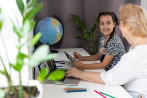 süß wenig Mädchen mit ihr Oma suchen beim Tablette beim Zuhause foto