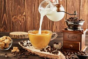 Gießen Kaffee von Glas Krug Milch in Glas Tasse mit Kaffee, Jahrgang Kaffee Schleifer und Klumpen Zucker auf hölzern Hintergrund foto