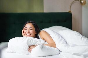 glücklich Morgens. schön Koreanisch Frau Lügen im Bett, lächelnd, aufwachen oben optimistisch, Startseite Sie selber mit warm Bettdecke foto