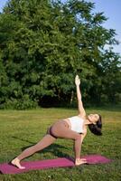 Vertikale Schuss von jung Koreanisch Frau tun Yoga Ausbildung auf Gummi Matte, Herstellung Asana Übungen auf frisch Luft im Park foto