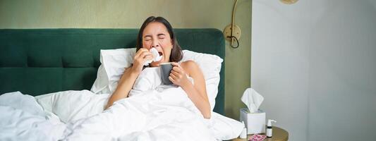 Gesundheit und Personen. asiatisch Mädchen Lügen im Bett, Gefühl krank, Niesen und Trinken heiß Tee, fangen kalt, bleiben beim Zuhause auf verlassen foto