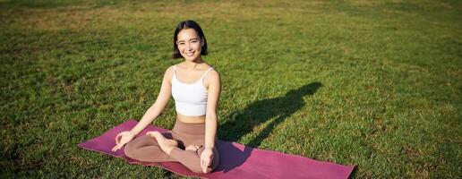 Achtsamkeit und Meditation. jung asiatisch Frau lächelnd während tun Yoga, entspannend im Asana auf Gummi Matte, tun Übungen im Park auf frisch Luft foto