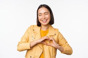 Bild von schön asiatisch Mädchen zeigen Herz, Liebe Zeichen, ausdrücken Pflege und romantisch Gefühle, Stehen Über Weiß Studio Hintergrund foto