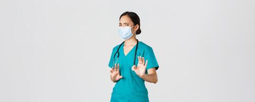 COVID-19, Coronavirus Krankheit, Gesundheitswesen Arbeitskräfte Konzept. unzufrieden asiatisch weiblich Arzt, Arzt oder Krankenschwester vermeiden Kontakt mit Keime, tragen medizinisch Maske und Peelings, zittern Hände Ablehnung foto