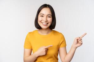 erstaunt jung asiatisch Frau, zeigen Werbung beiseite, zeigen Finger richtig beim Beförderung Text, Marke Logo, Stehen glücklich gegen Weiß Hintergrund foto