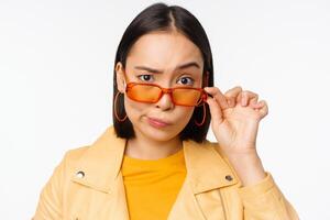 Bild von jung asiatisch stilvoll Frau, suchen von unter Sonnenbrille mit skeptisch, Unglaube Gesicht, ausdrücken zweifeln, Stehen Über Weiß Hintergrund foto