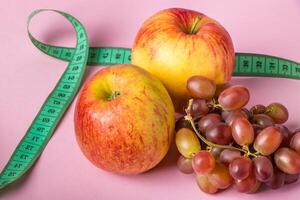 frisches Obst und Maßband auf rosa Hintergrund. das konzept der ernährung und der gesunden ernährung. foto