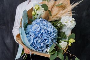 ein Mädchen im ein Weiß Hemd hält ein groß Strauß mit Blau Hortensie und andere Blumen. das Strauß ist eingewickelt im farbig Papier. Geschenk zum das Lehrer zum das zuerst von September. foto