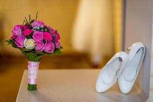 Hochzeit Weiß Schuhe und Strauß von Rosa und lila Rosen. Braut- Fototermin. Nahaufnahme. foto