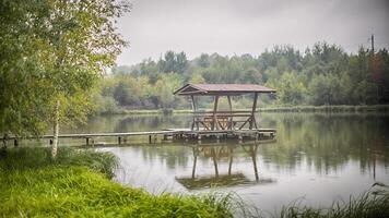 Pavillon mit Stühle und ein Tabelle steht auf ein hölzern Mauerwerk im das Mitte von das See foto