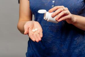 jung Frau gießt das Tabletten aus von das Flasche in ihr Hand. weiblich Hand halten ein Medizin und verschütten Tabletten aus von das Krug. Nahansicht foto