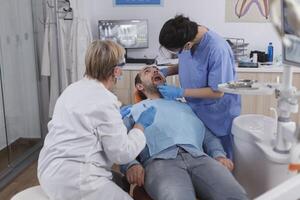 Zahnarzt Frau Krankenschwester Überprüfung geduldig Mund Analysieren Zähne Infektion mit stomatologisch bohren Instrument während kieferorthopädisch Untersuchung im Dental Büro Zimmer. Konzept von Zahnheilkunde Verfahren foto