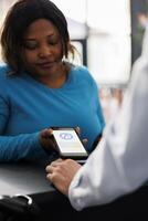 afrikanisch amerikanisch Käufer Kauf Kleider mit Telefon nfc Zahlung, mit Smartphone beim pos Terminal im modern Boutique speichern. Frau bezahlen zum modisch beiläufig tragen und Zubehör beim Schalter. schließen hoch. foto