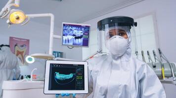 Arzt zeigen Digital Röntgen auf Tablette im Dental Büro mit Neu normal, erklären Zähne Behandlung. Stomatologie tragen schützend passen gegen Infektion mit Coronavirus zeigen beim Radiographie. foto