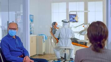 Menschen mit Schutz Masken diskutieren im Rezeption Bereich warten Arzt im Dental Klinik während Stomatologe Arbeiten im Hintergrund tragen ppe Anzug. Konzept von Neu normal Zahnarzt Besuch foto