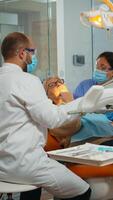 Zahnarzt Behandlung Zähne zu Senior Frau geduldig im Klinik Lügen auf Stuhl mit öffnen Mund. Arzt und Krankenschwester Arbeiten zusammen im modern stomatologisch Büro tragen Schutz Maske foto