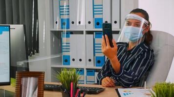 Unternehmer tragen Gesicht Schutz gegen Coronavirus mit Telefon zum Videotreffen reden mit entfernt Mitarbeiter Sitzung im Neu normal Büro korporativ Gebäude. Frau respektieren Sozial Entfernung foto