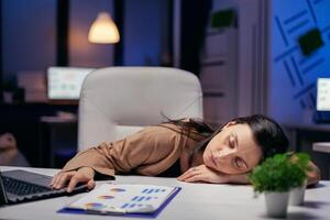 müde Geschäftsfrau ruhen Kopf auf Schreibtisch halten Hand auf Laptop. Mitarbeiter fallen schlafend während Arbeiten spät beim Nacht allein im das Büro zum wichtig Unternehmen Projekt. foto