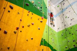 sportlich wenig Mädchen Klettern künstlich Felsbrocken auf praktisch Mauer im Fitnessstudio foto