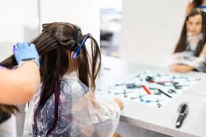 wenig Mädchen Farbstoffe ihr Haar lila im ein Friseur Salon foto