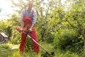 Mähen Gras mit elektrisch Rasen Mäher. Garten Arbeit Konzept. Mann mäht das Gras mit Hand Mäher im das Garten foto