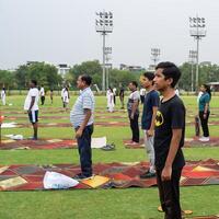 Neu Delhi, Indien, Juni 21, 2023 - - Gruppe Yoga Übung Session zum Menschen beim Yamuna Sport Komplex im Delhi auf International Yoga Tag, groß Gruppe von Erwachsene Teilnahme Yoga Klasse im Kricket Stadion foto