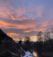 ein schön Sonnenuntergang Über ein Fluss mit Schnee auf das Boden foto
