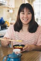 asiatisch Frau Essen Reis mit Essstäbchen sieht aus und lächelt beim Kamera. foto