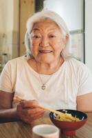 Senior Erwachsene japanisch Frau Essen Reis mit Essstäbchen sieht aus und lächelt beim Kamera foto