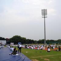 Neu Delhi, Indien, Juni 21, 2023 - - Gruppe Yoga Übung Session zum Menschen beim Yamuna Sport Komplex im Delhi auf International Yoga Tag, groß Gruppe von Erwachsene Teilnahme Yoga Klasse im Kricket Stadion foto