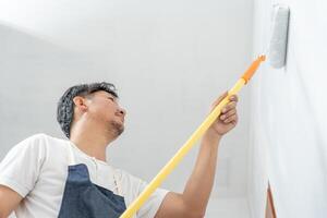 Maler Mann, Bürste im Hand zum Produkte zu wiederherstellen und Farbe das Wand, Innen- das Gebäude Seite? ˅ von ein Haus, Mauer während malen, Renovierung, malen, Auftragnehmer, Architekt, Konstruktion Arbeiter foto