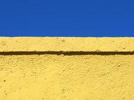 ai generiert ein Gelb Zement Mauer mit ein Blau Himmel im das Hintergrund foto