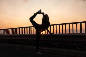 Schönes junges brünettes Mädchen, das bei Sonnenuntergang eine Straße mitten auf dem Feld aufwirft, Ballett, Silhouette foto