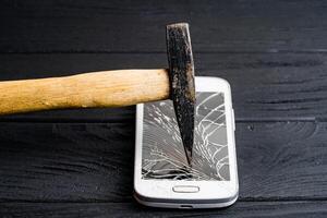 Hammer bricht modern sensorisch Smartphone isoliert auf dunkel Hintergrund. teuer Handy zerschlagen durch groß Hammer auf das hölzern Oberfläche. foto