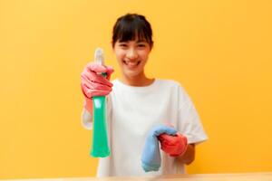 glücklich asiatisch Frau Reinigung halten Reinigung Ausrüstung Gelb Hintergrund. Hausfrau halten Reinigung Ausrüstung. foto