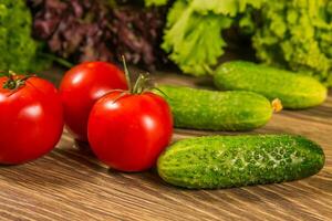 frisch Gemüse. Tomaten und Gurken auf ein hölzern Tisch. Grün Salat im das Hintergrund. foto