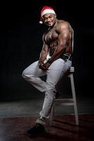 Bodybuilder posieren wie Santa Klaus. afrikanisch amerikanisch Mann mit Weihnachten Hut und nackt Abs. muskulös Körper Typ. foto